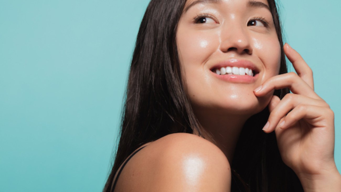 Close up of cute asian girl with glowing skin against blue background. Beautiful face of girl with fresh healthy skin.